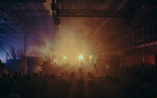 Crowded indoor music event with lively crowd under dramatic lighting and smoke effects.