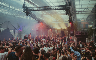 Crowd enjoying music at a lively indoor concert with colorful stage lighting and smoke effects.