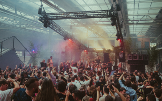 Crowd enjoying an indoor music festival with lights and raised hands in the air.